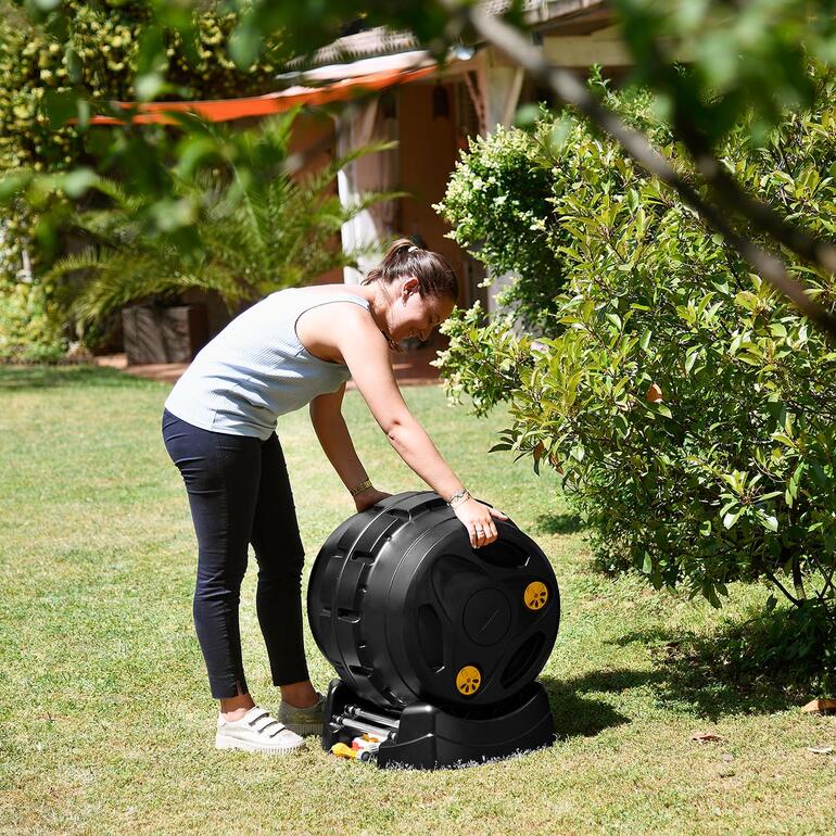 Femme debout sur l'herbe en train de déplacer un composteur à tambour 2-en-1.