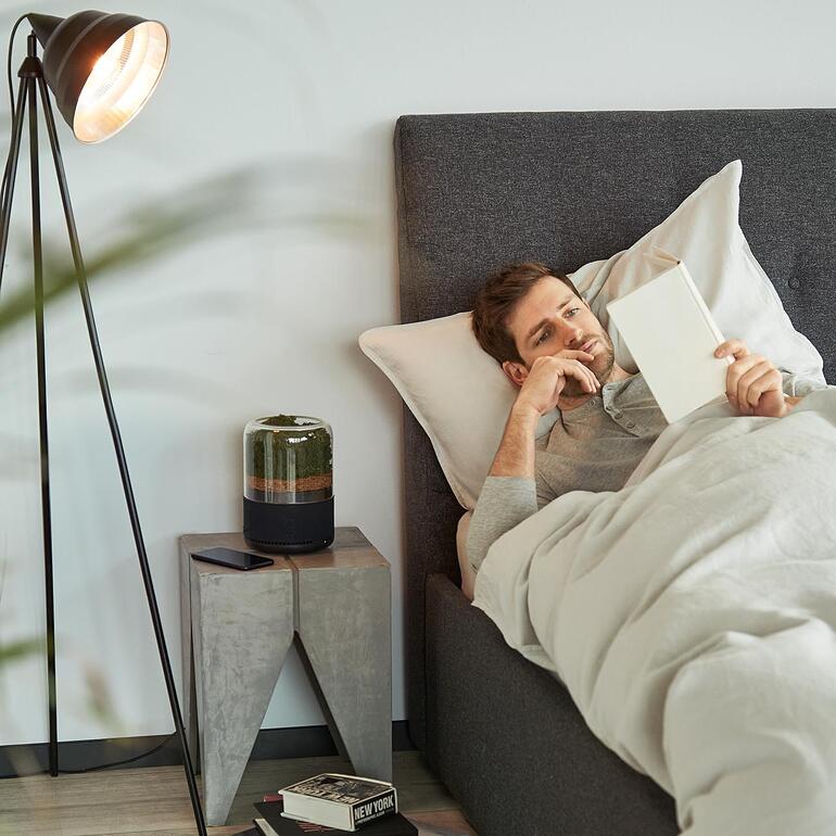 Assainisseur d’air naturel Homme au lit lit un livre à côté d'un purificateur d'air naturel.