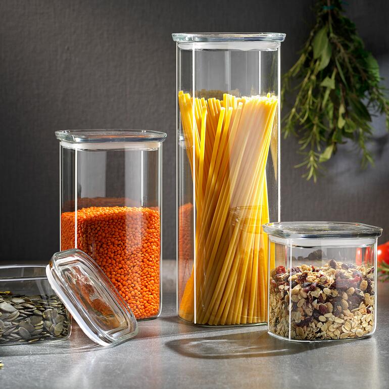 Bocaux de stockage avec couvercle en verre, remplis de lentilles, de spaghetti et de muesli sur une table.