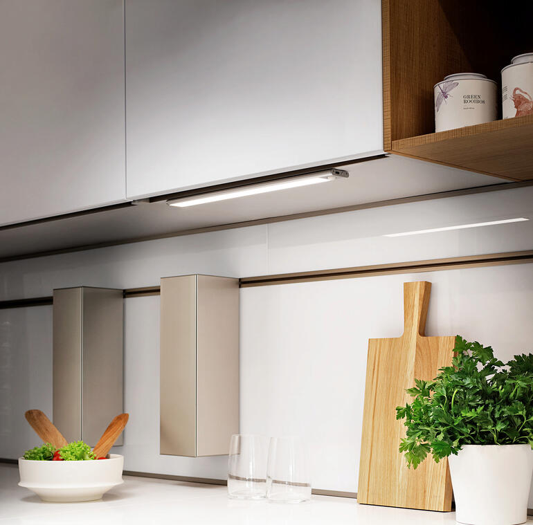 Barre lumineuse rechargeable montée sous un meuble de cuisine avec des ingrédients frais sur le plan de travail.