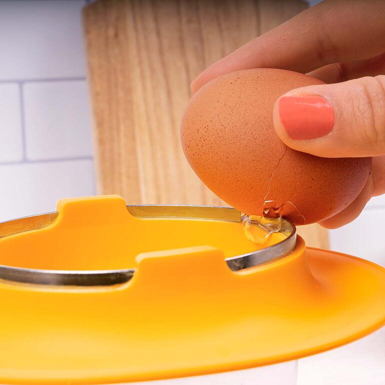 Vous cassez les œufs proprement sur le fin rebord en inox – sans briser la coquille. Démonstration avec la main cassant un œuf dans un séparateur d'œufs orange.