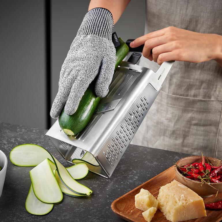 Les lames découpées au laser coupent les aliments très facilement et de manière précise. Main utilisant une râpe verticale pour râper une courgette.