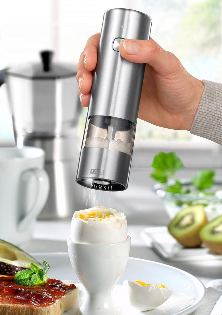 Main tenant un moulin à épices à batterie au-dessus d'un œuf à la coque.