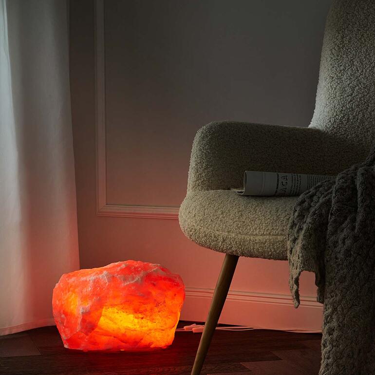 Lampe en cristal de sel émettant une lumière chaleureuse à côté d'un fauteuil confortable.