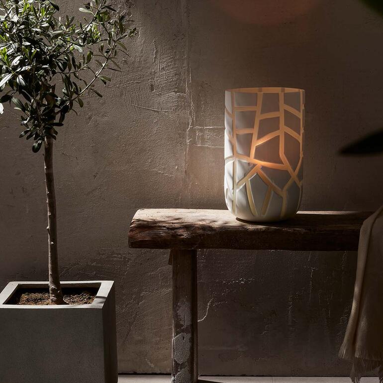 Utilisable de manière variée, en tant que vase ou photophore. Vase sur une table, éclairée, avec des découpes décoratives