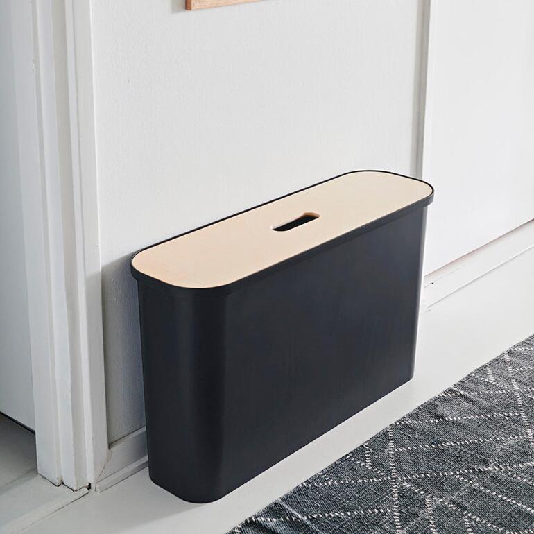 Conteneur de rangement noir avec couvercle clair, adossé à un mur.