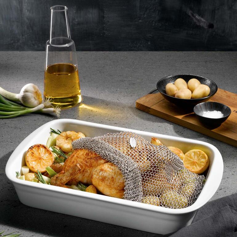 Poulet dans un panier à rôtir sur une plaque avec des légumes et de l'huile.