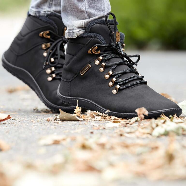 Avec ces bottines à lacets, chaudes pour l’hiver, vous apprécierez la sensation d’une marche pieds-nus, libératrice et naturelle, même lors de journées froides – dans vos activités quotidiennes, pour une sortie shopping ou en ville, une balade en forêt … Bottes d'hiver noires avec détail doré et lacets sur un sol gris.