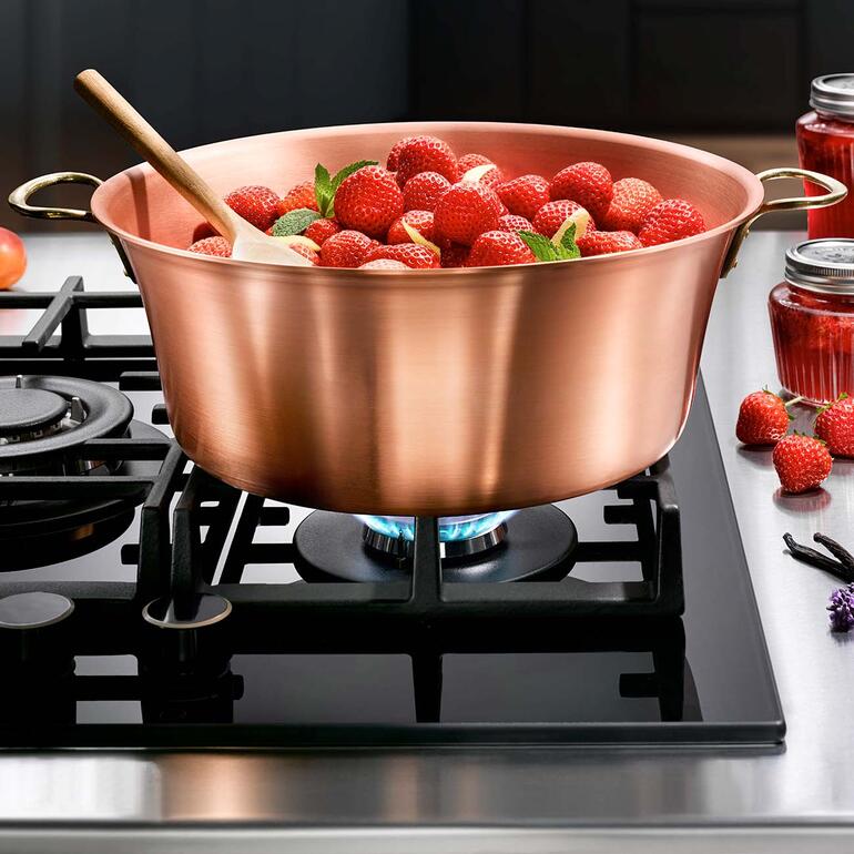 Casserole en cuivre avec des fraises fraîches sur le feu avec une cuillère en bois.