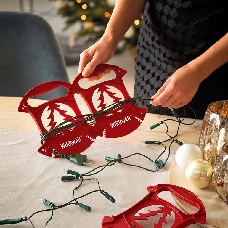 Utilisables seuls ou ensemble, grâce au système de rangement breveté. Personne enroulant des lumières de Noël avec enrouleur WIRRwAR sur une table.