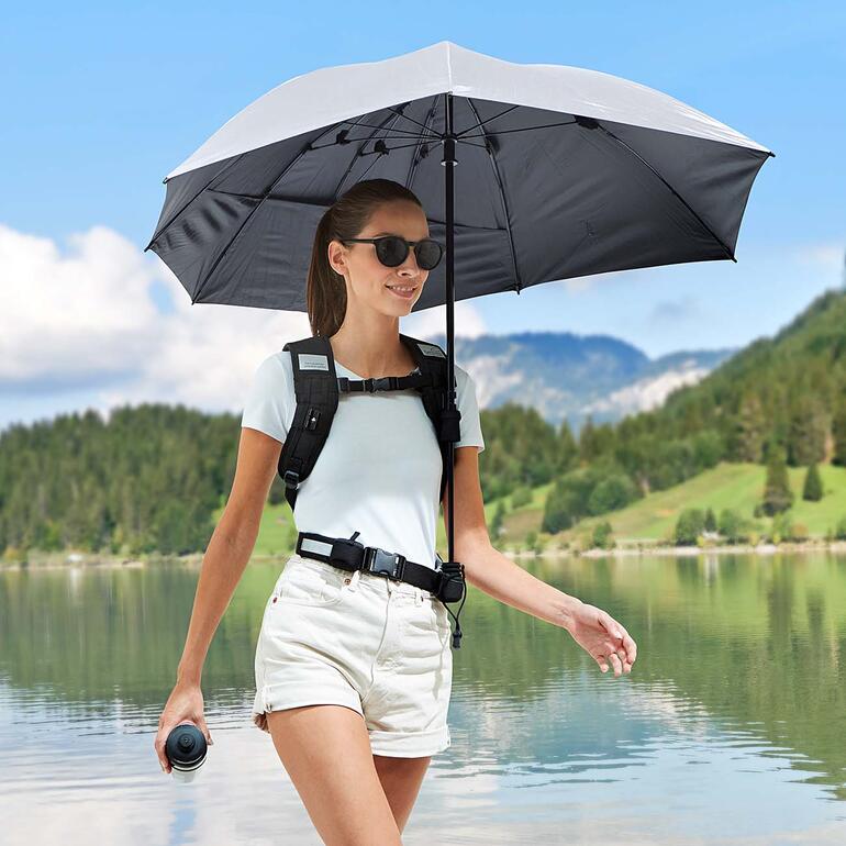 Femme avec parapluie à dos mains libres près d'un lac.