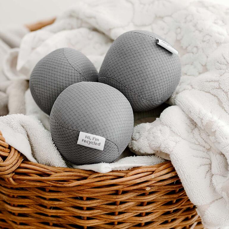 Trois balls antistatiques de séchage gris dans un panier à linge.