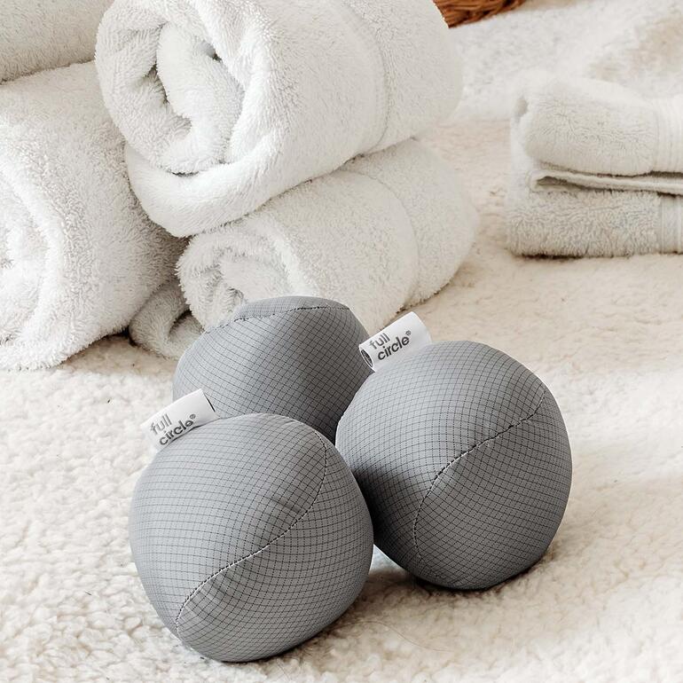 Balles de séchage antistatiques, lot de 3 pièces Trois balles de séchage grises à côté de serviettes blanches.