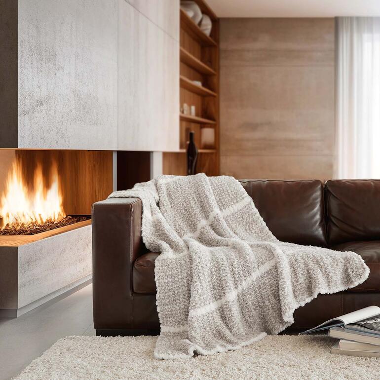 Couverture en tricot en fausse fourrure sur un canapé marron devant une cheminée.