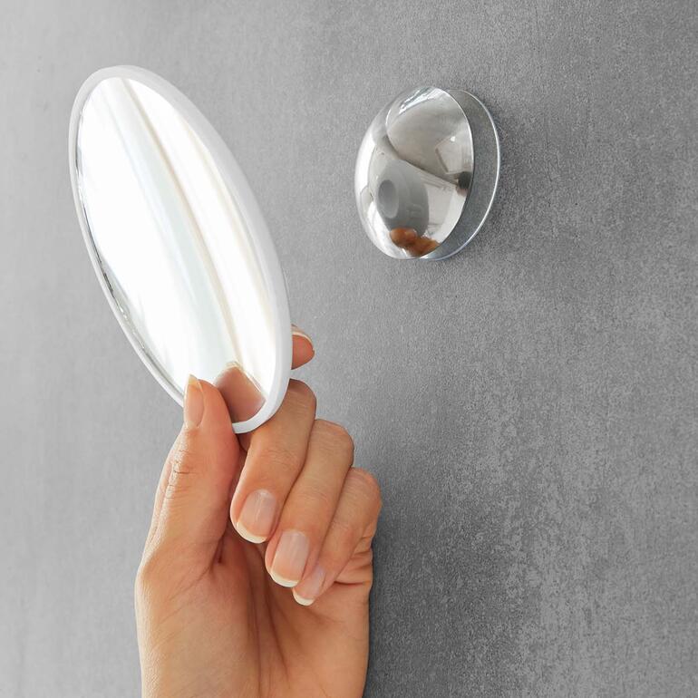 Une main tient un miroir à main ovale près d'un miroir mural.