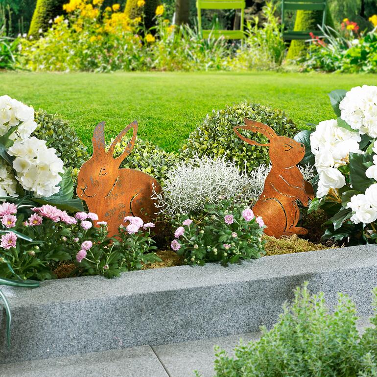 Deux piquets de jardin en forme de lapins en métal placés dans un parterre de fleurs.