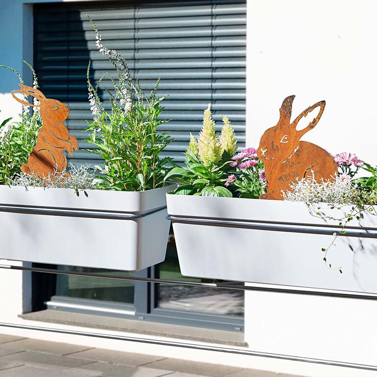 Piquets de jardin en forme de lapins dans des pots de fleurs sur un balcon.