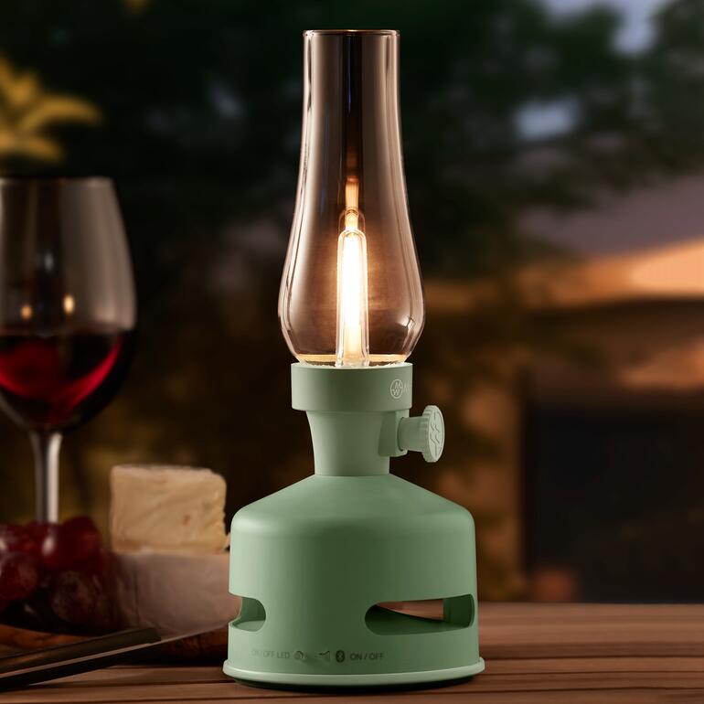 Lampe à huile LED en vert menthe avec une bougie en extérieur sur une table.