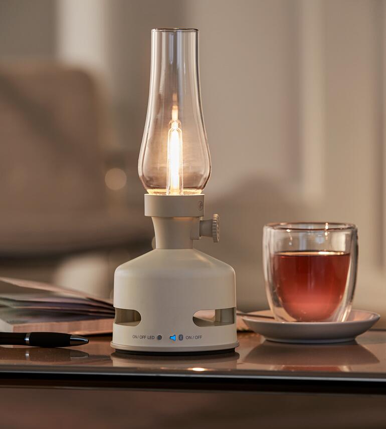 Avec enceinte Bluetooth intégrée pour ajouter un son puissant. Lampe à huile LED couleur crème sur une table avec un verre de thé.