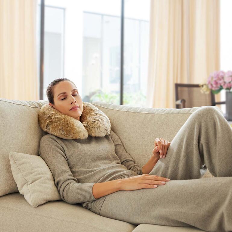 Femme détendue avec un coussin de cou en fausse fourrure sur le canapé