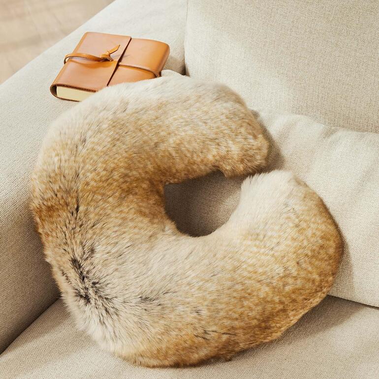 Coussin de cou en fausse fourrure sur un canapé à côté d'un livre
