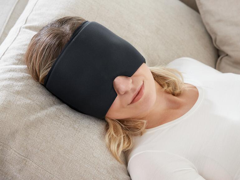Femme avec une compresse noire sur les yeux se détend sur un canapé.