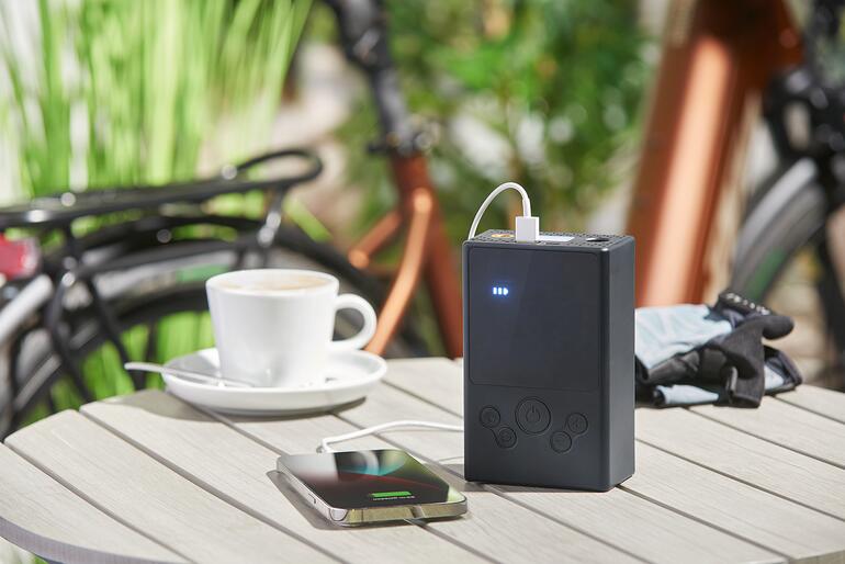 Compresseur à air rechargeable charge un smartphone sur une table.