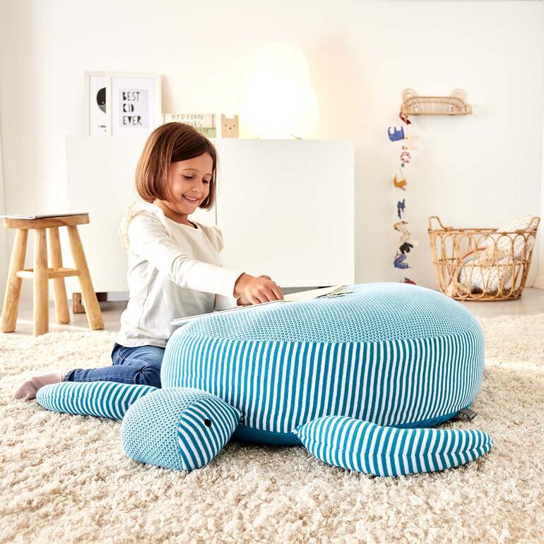 Fille avec un livre assise sur une tortue câline/siege dans une pièce cozy.