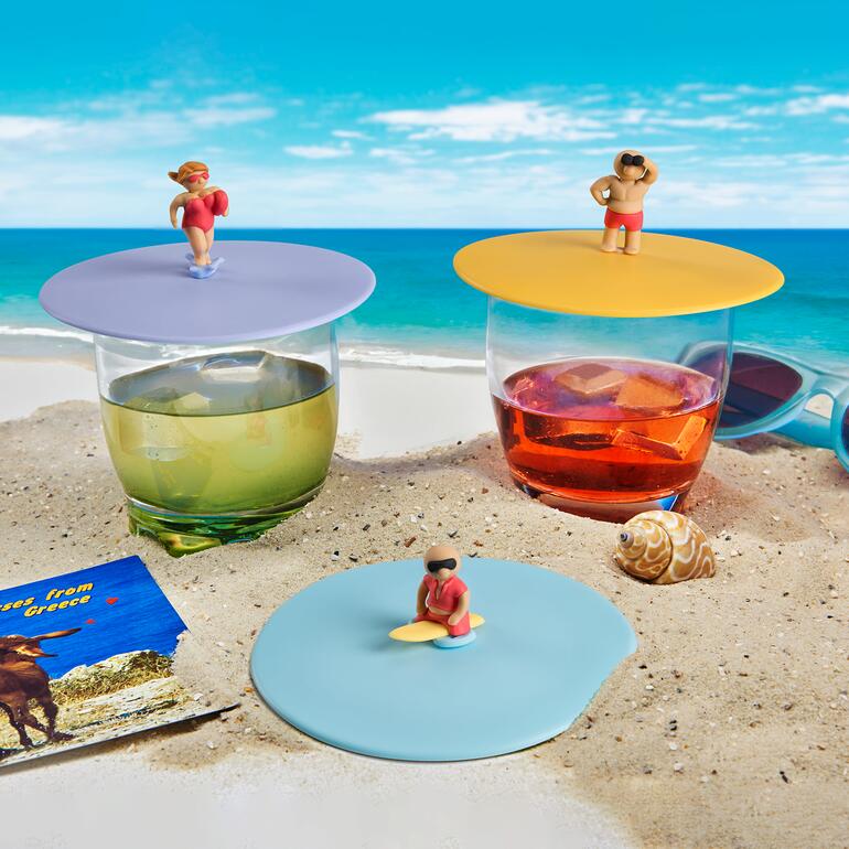Trois couvercles en verre avec des figurines de surfeurs sur une plage de sable.
