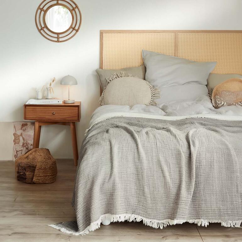 Idéal également en tant que jeté de lit léger. Couverture en mousseline grise sur un lit avec tête de lit et coussins.