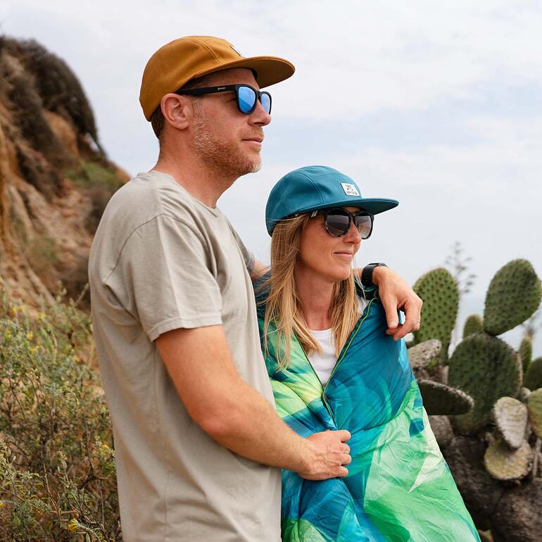 Couple posant avec la couverture de voyage recyclée 3-en-1 et des lunettes de soleil