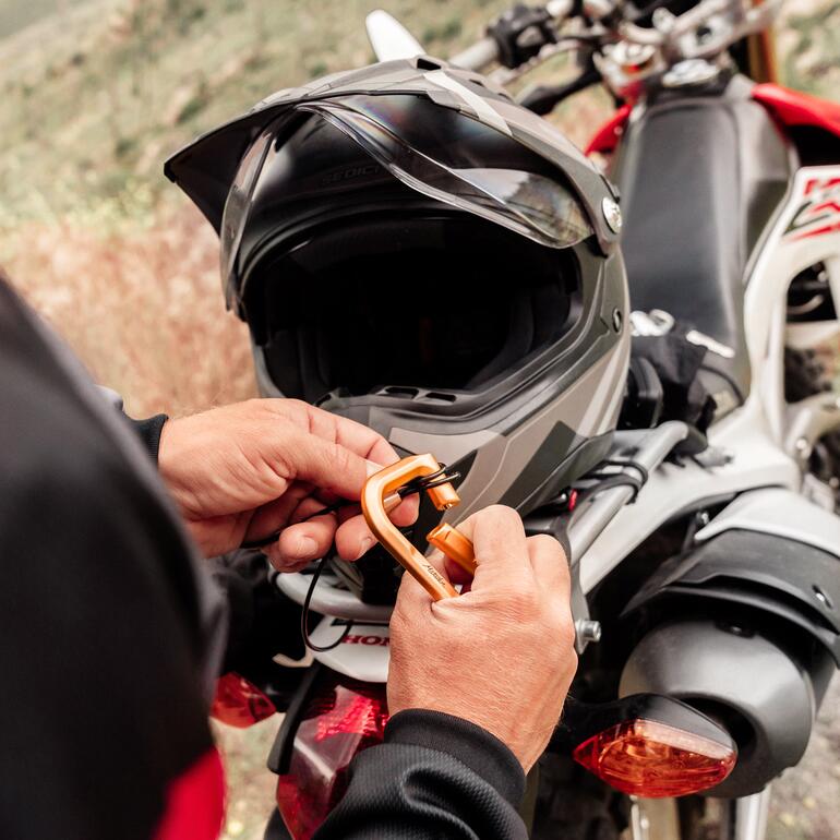 Une personne fixe un mousqueton avec serrure sur un casque de moto.