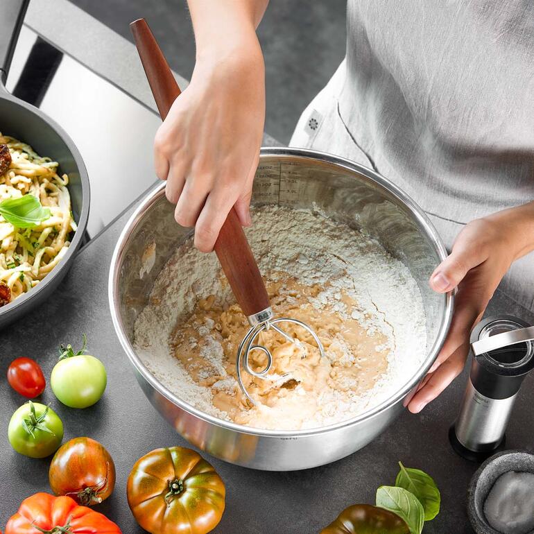 Des mains utilisent un fouet danois dans un bol de pâte.