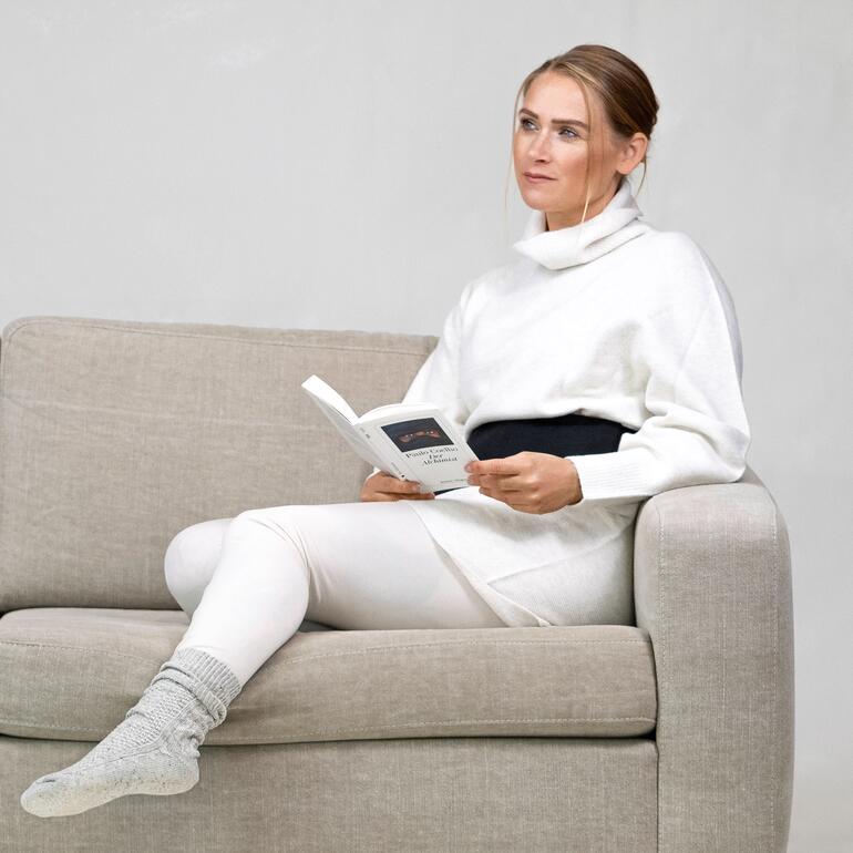 Avec ceinture élastique confortable en 2 tailles (coussin de tourbe pour dos & ventre). Femme avec un coussin de tourbe autour de la taille, lisant un livre