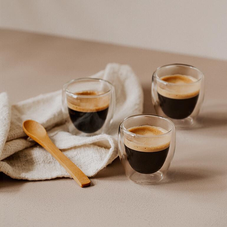 Espresso (80 ml, 6,5 cm H) Trois verres thermiques pour espresso élégants avec de l'espresso frais sur une table.