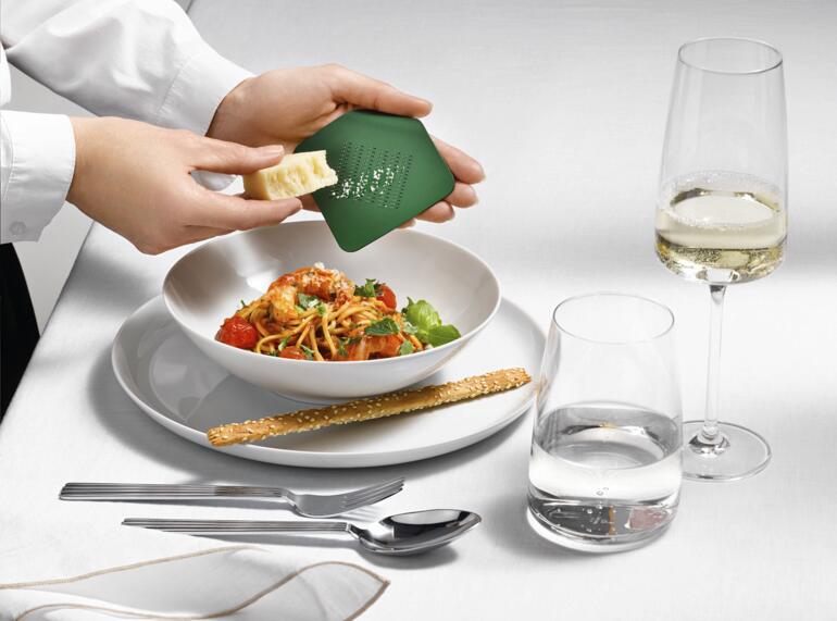 Personne tenant une râpe design Irogami au-dessus d'une assiette de salade de pâtes.