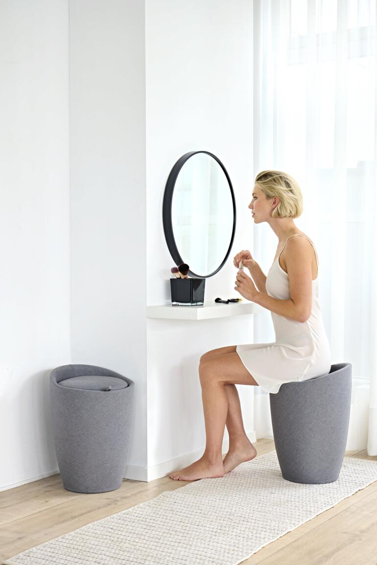Femme assise sur un panier à linge avec un tabouret devant un miroir.