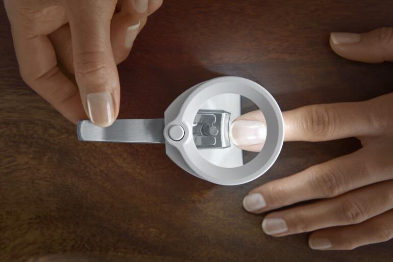Grâce à la lentille grossissante 3,5x et à la lumière LED, votre ongle est toujours clairement visible – chaque coupe est sûre et précise. Main tenant un coupe-ongles sécurisé au-dessus d'un doigt