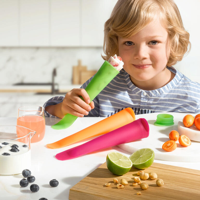Enfant mignon avec glace dans un moule en silicone, entouré de fruits