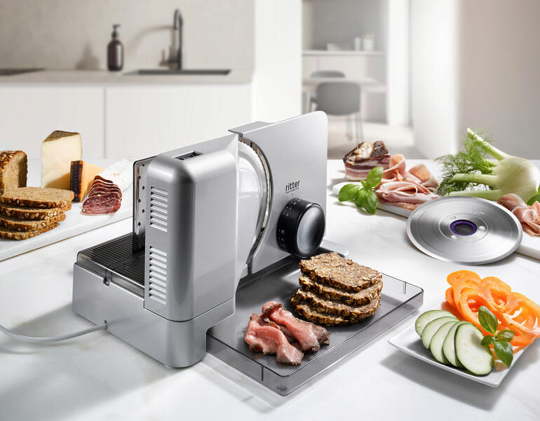 Trancheuse Duo Plus coupe du pain et de la charcuterie sur un plan de travail.