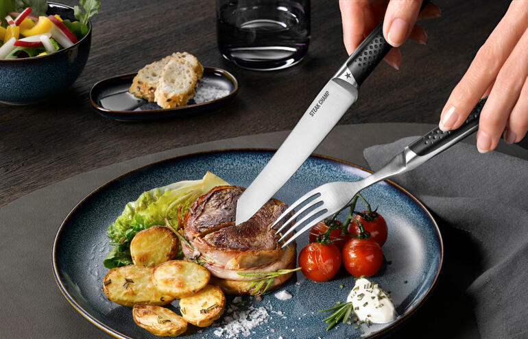 En raison de la forme incurvée de la lame, seule la pointe du couteau entre en contact avec l’assiette lors de la coupe, ainsi il garde son tranchant beaucoup plus longtemps. Main utilisant des couverts à steak Prime Rib pour couper un steak dans une assiette.
