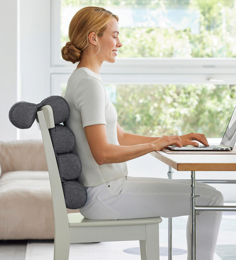 Femme assise avec un coussin flexible à un bureau, travaillant sur un ordinateur portable.