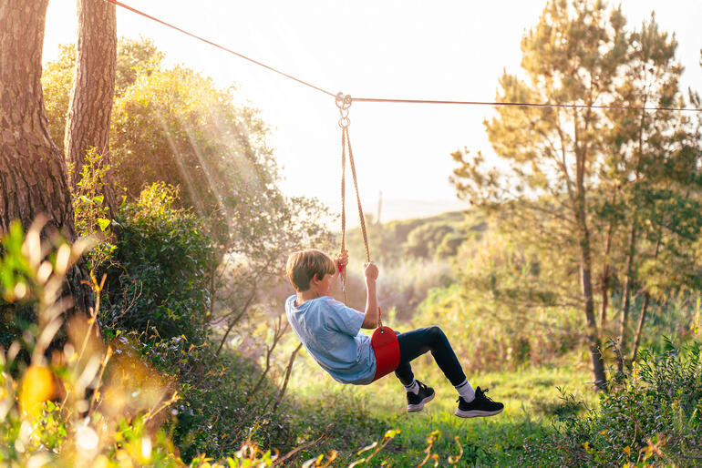 Se balancer dʼarbre en arbre avec la tyrolienne sur le siège oscillant réglable en hauteur est extrêmement amusant. Garçon se balançant sur une corde dans un parcours extérieur au coucher du soleil.