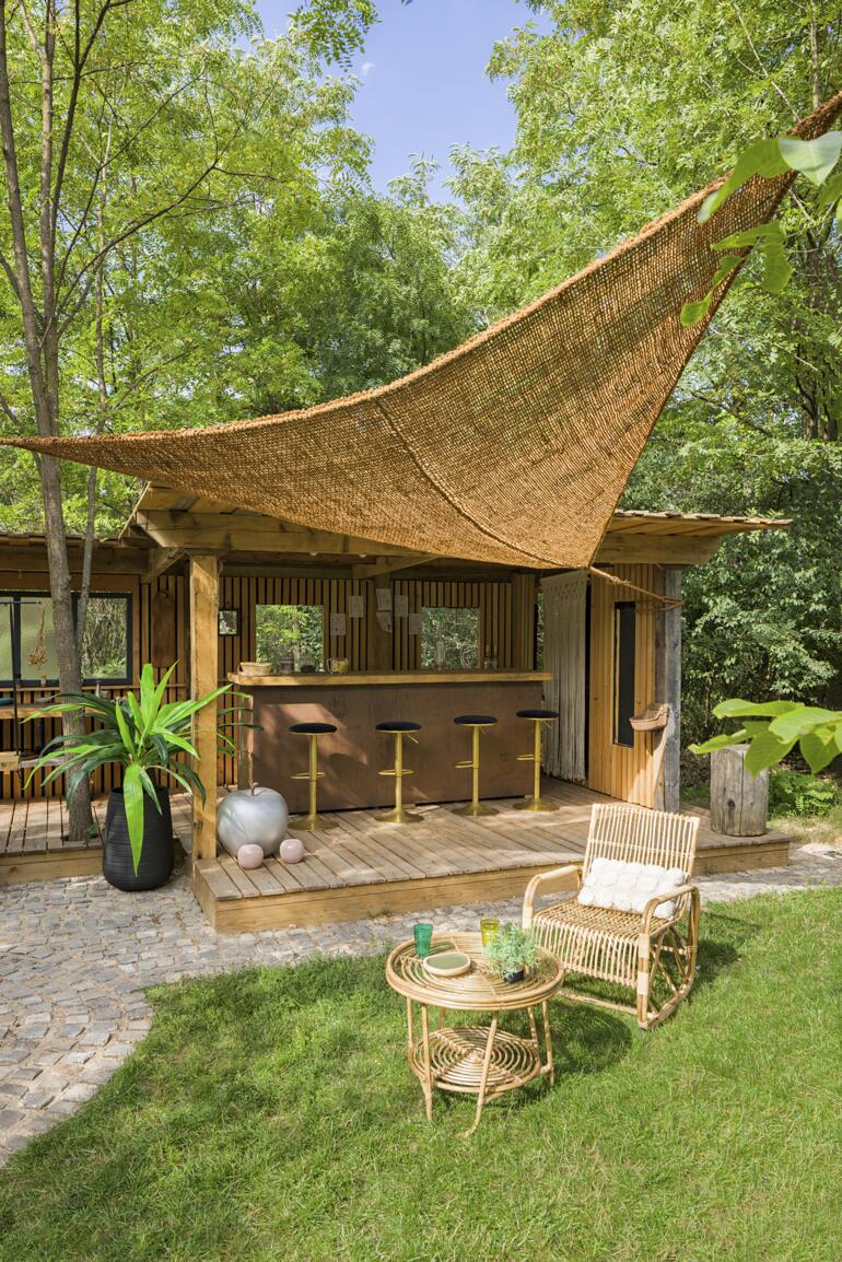Voile solaire en fibres de coco au-dessus d'une terrasse en bois avec des tabourets de bar.