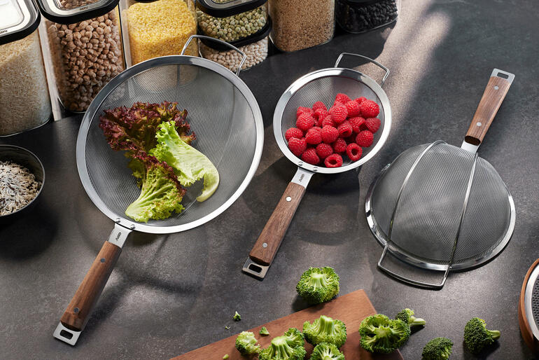 Trois passoires avec des poignées en bois sur une table de cuisine.