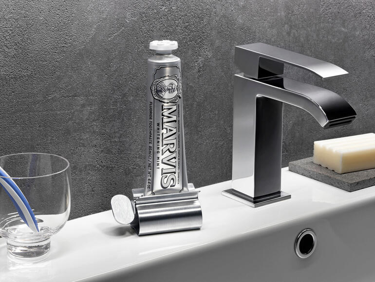 Presse-tube en acier inoxydable avec un tube de dentifrice à côté d'un robinet.