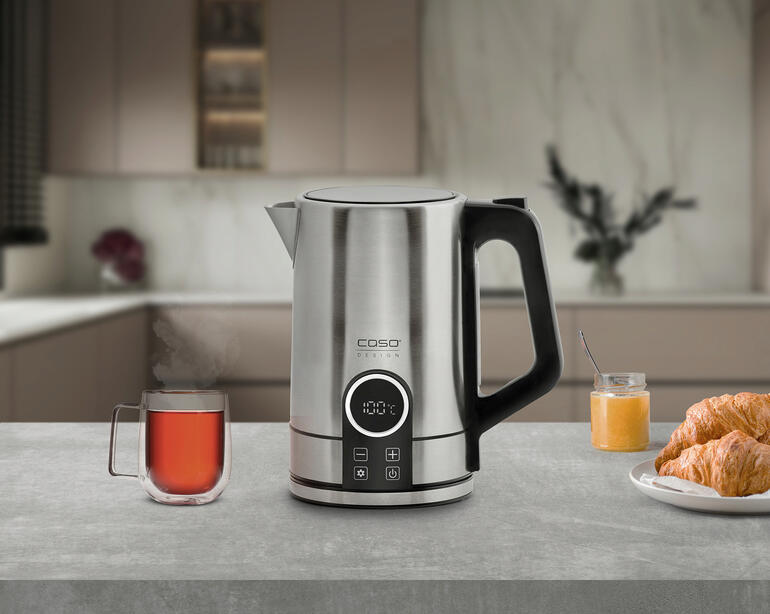 Bouilloire en acier inoxydable moderne sur un plan de travail avec une tasse de thé et un croissant.