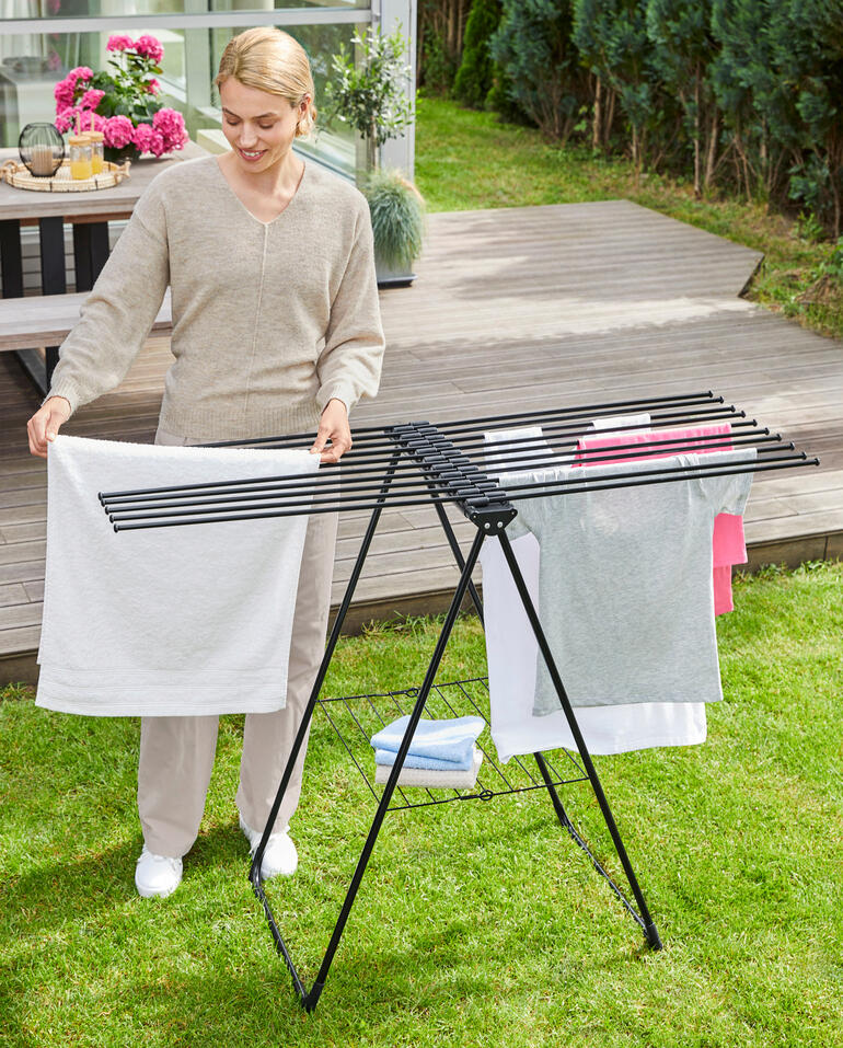 Grâce à sa forme sans cadre, le linge peut être aisément glissé par les côtés ouverts sur les tiges rondes de 4 mm d’épaisseur. Femme suspendant du linge sur un étendoir à linge design moderne dans le jardin