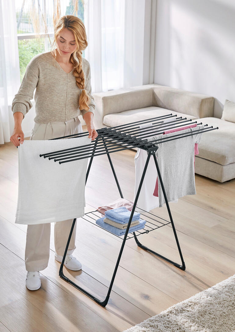 Femme organisant du linge sur un étendoir à linge design dans le salon
