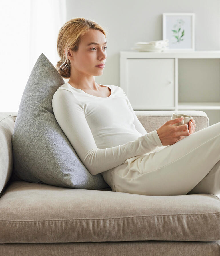 Femme avec un coussin de dos gris assise détendue sur un canapé.